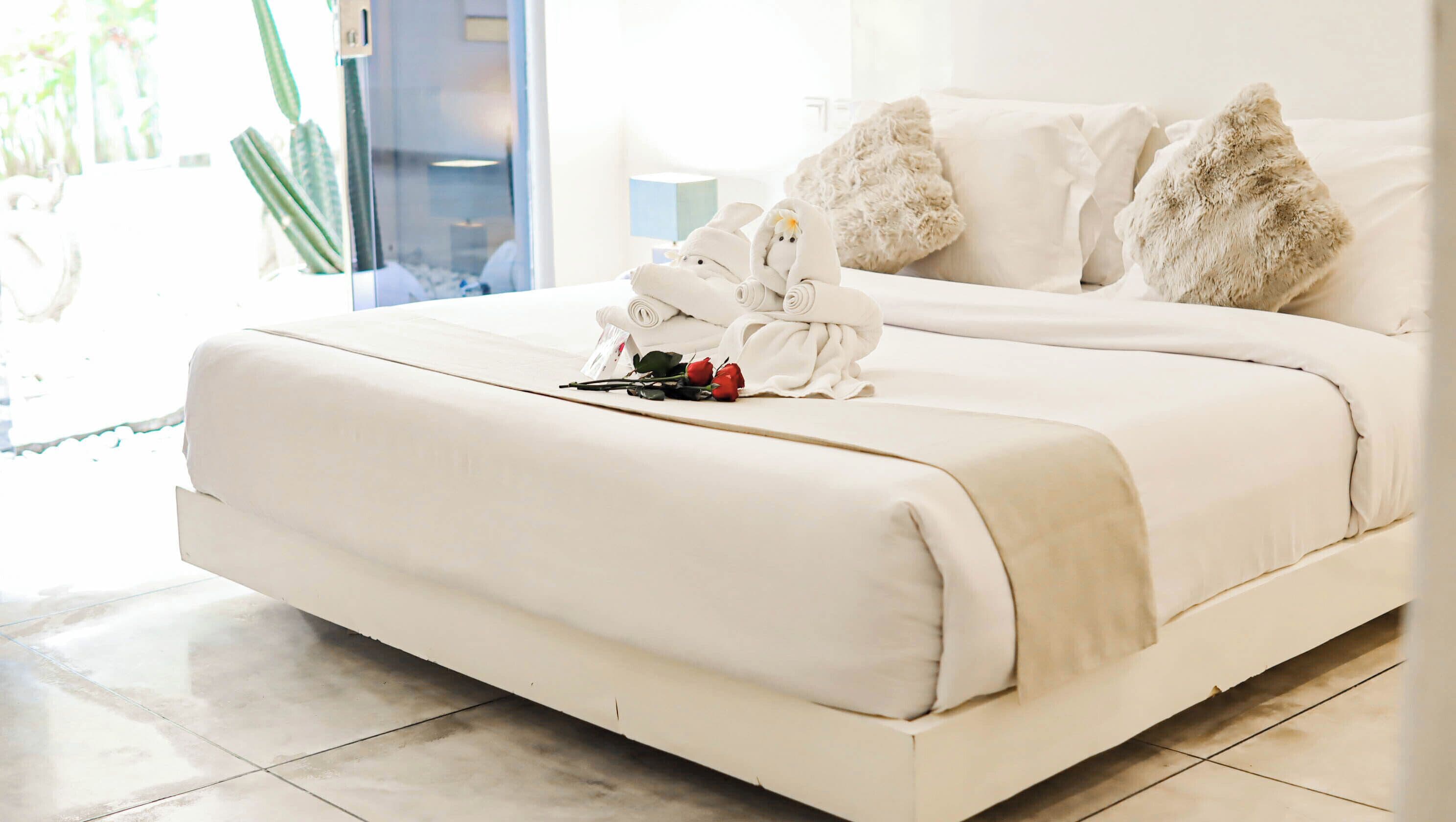 A hotel room with a large bed, fluffy pillows, and a bouquet of red roses.