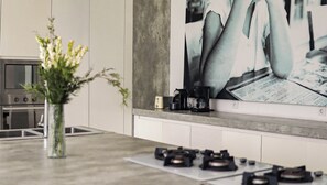 A kitchen with a modern design, featuring a gas stove, a coffee maker, and a toaster on the countertop. - Calma Cliff Villas  (Ungasan)