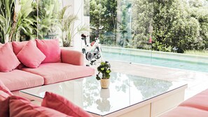 Sala de estar moderna com um sofá rosa, uma mesa de centro de vidro e vista para uma piscina.