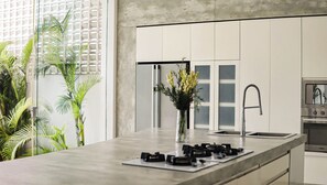 A modern kitchen with a large island, stainless steel appliances, and a view of greenery outside. - Calma Cliff Villas  (Ungasan)