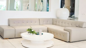 A beige sectional sofa with a white round coffee table in front, a vase with flowers, and a large white vase on a table in the background. - Calma Cliff Villas  (Ungasan)