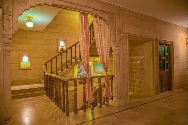 Un escalier avec une rampe en bois, un mur en pierre et une porte dotée d’un vitrail vert.
