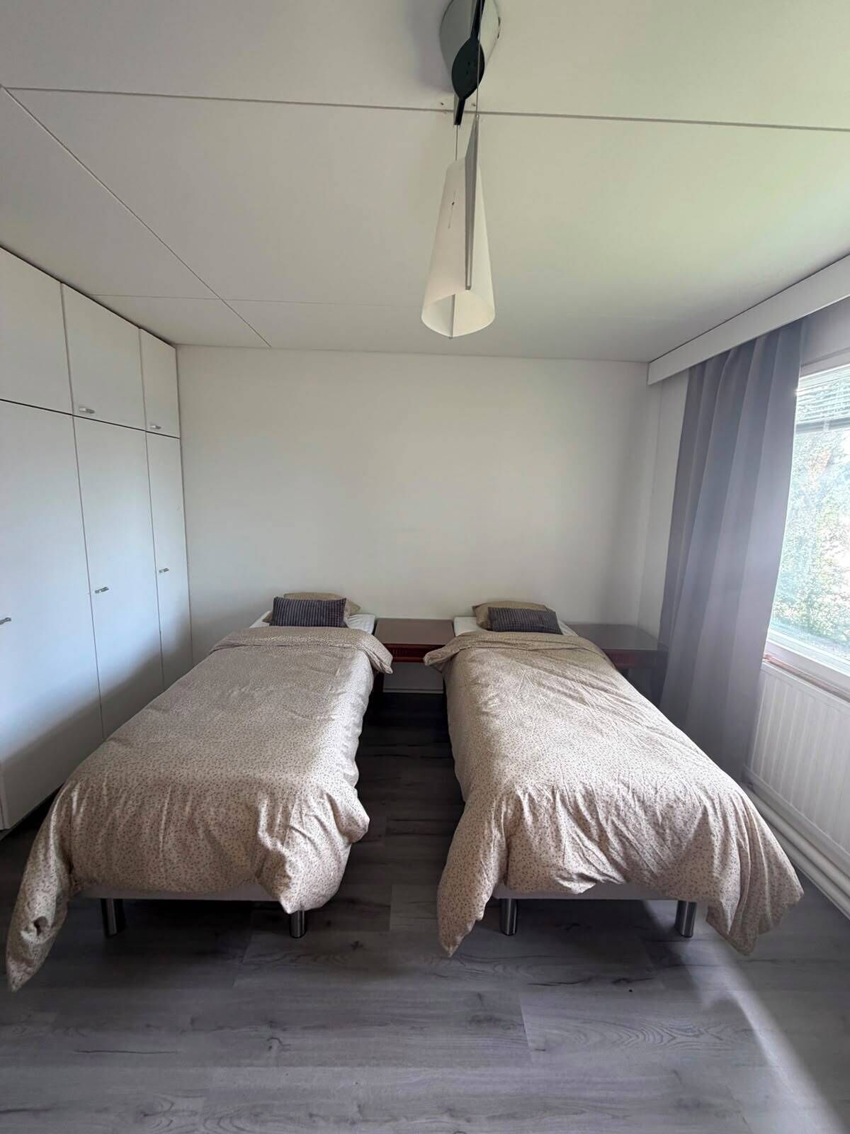 Une chambre avec deux lits, une armoire et une fenêtre avec des rideaux.