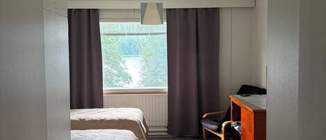 A hotel room with two beds, a desk, and a window with curtains.