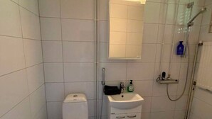 Un baño pequeño con azulejos, inodoro, lavamanos y ducha.