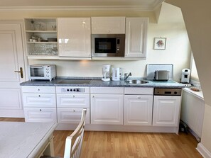 A compact kitchen with white cabinetry, a microwave, a toaster, a coffee maker, and a sink. - Süderstra ße 29a, Apt. 02 - 3-room upper-floor vacation apartment with a south-facing balcony for (Sylt-Ost)
