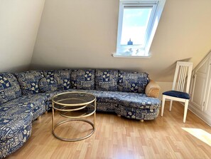 A corner room with a blue patterned sofa, a round glass coffee table, and a white chair. - Süderstraße 29a, Apt. 02 - 3-room upper-floor vacation apartment with a south-facing balcony for (Sylt-Ost)