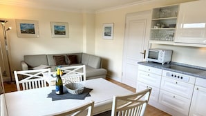 A kitchen with white cabinets, a dining table with chairs, and a white countertop with a toaster. - Süderstraße 29a, Apt. 02 - 3-room upper-floor vacation apartment with a south-facing balcony for (Sylt-Ost)