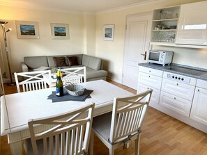 A kitchen with white cabinets, a dining table with chairs, and a white countertop with a toaster. - Süderstraße 29a, Apt. 02 - 3-room upper-floor vacation apartment with a south-facing balcony for (Sylt-Ost)