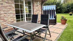 An outdoor patio with a table and chairs, a striped awning, and a brick wall. - Norderstraße, Apartment 1 - Cozy ground-floor vacation apartment with a fireplace and (Sylt)