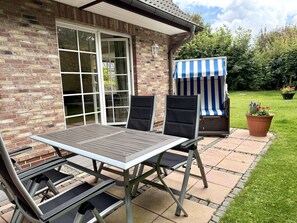 An outdoor patio with a table and chairs, a striped awning, and a brick wall. - Norderstraße, Apartment 1 - Cozy ground-floor vacation apartment with a fireplace and (Sylt)