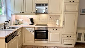 A kitchen with white cabinets, a stainless steel oven, a coffee maker, and a microwave. - Norderstraße, Apartment 1 - Cozy ground-floor vacation apartment with a fireplace and (Sylt)