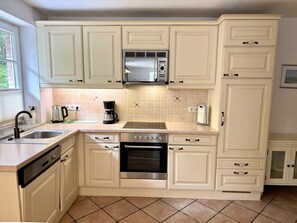 A kitchen with white cabinets, a stainless steel oven, a coffee maker, and a microwave. - Norderstraße, Apartment 1 - Cozy ground-floor vacation apartment with a fireplace and (Sylt)