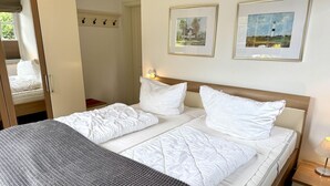 A neatly made bed with white linens, a gray throw blanket, and two framed pictures on the wall. - Norderstraße, Apartment 1 - Cozy ground-floor vacation apartment with a fireplace and (Sylt)