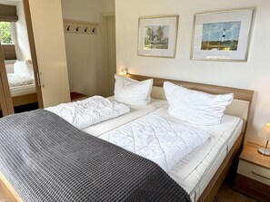 A neatly made bed with white linens, a gray throw blanket, and two framed pictures on the wall. - Norderstraße, Apartment 1 - Cozy ground-floor vacation apartment with a fireplace and (Sylt)