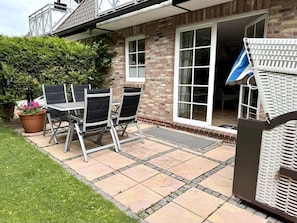 A patio with a table and chairs, a potted plant, and a white wicker chair. - Norderstraße, Apartment 1 - Cozy ground-floor vacation apartment with a fireplace and (Sylt)