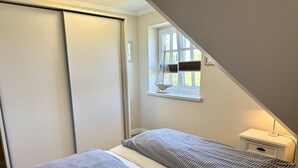 A bedroom with a bed, a nightstand, a window, and a door. - Eidumweg Apartment 4 - Bright and modern upper-floor apartment for 4 people with (Sylt)