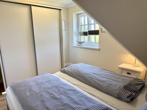 A bedroom with a bed, a nightstand, a window, and a door. - Eidumweg Apartment 4 - Bright and modern upper-floor apartment for 4 people with (Sylt)
