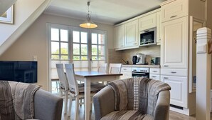 A modern kitchen with white cabinetry, a dining table with chairs, and a TV mounted on the wall. - Eidumweg Apartment 4 - Bright and modern upper-floor apartment for 4 people with (Sylt)