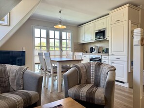 A modern kitchen with white cabinetry, a dining table with chairs, and a TV mounted on the wall. - Eidumweg Apartment 4 - Bright and modern upper-floor apartment for 4 people with (Sylt)