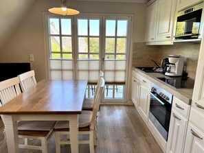 A kitchen with a wooden table, white chairs, a coffee maker, and a stove. - Eidumweg Apartment 4 - Bright and modern upper-floor apartment for 4 people with (Sylt)
