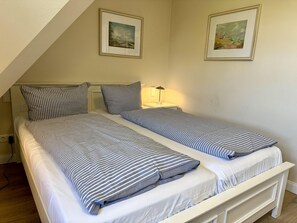 A bedroom with two single beds, a nightstand, a lamp, and two framed pictures on the wall. - Eidumweg Apartment 4 - Bright and modern upper-floor apartment for 4 people with (Sylt)