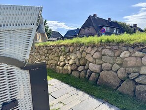 Eine Steinmauer mit Metallkonstruktion darüber, ein gepflasterter Weg und Häuser im Hintergrund.