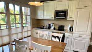 A kitchen with white cabinetry, a wooden dining table, and chairs. - Eidumweg Apartment 4 - Bright and modern upper-floor apartment for 4 people with (Sylt)