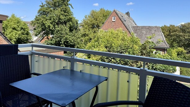A balcony with a table and chairs, overlooking a residential area with houses and trees. - Eidumweg Apartment 4 - Bright and modern upper-floor apartment for 4 people with (Sylt)