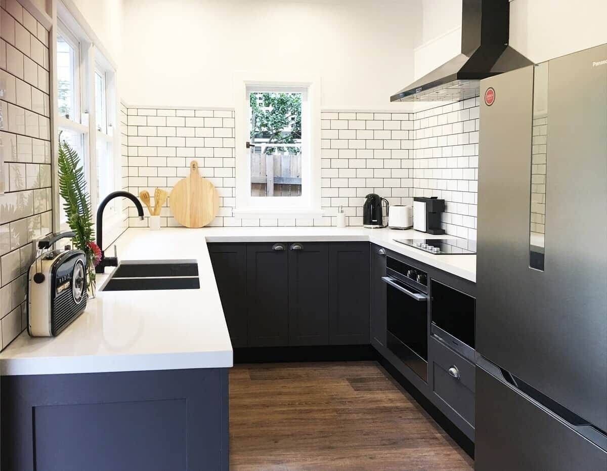 A modern kitchen with a central island, black cabinets, a stainless steel refrigerator, and a window with a view of greenery.