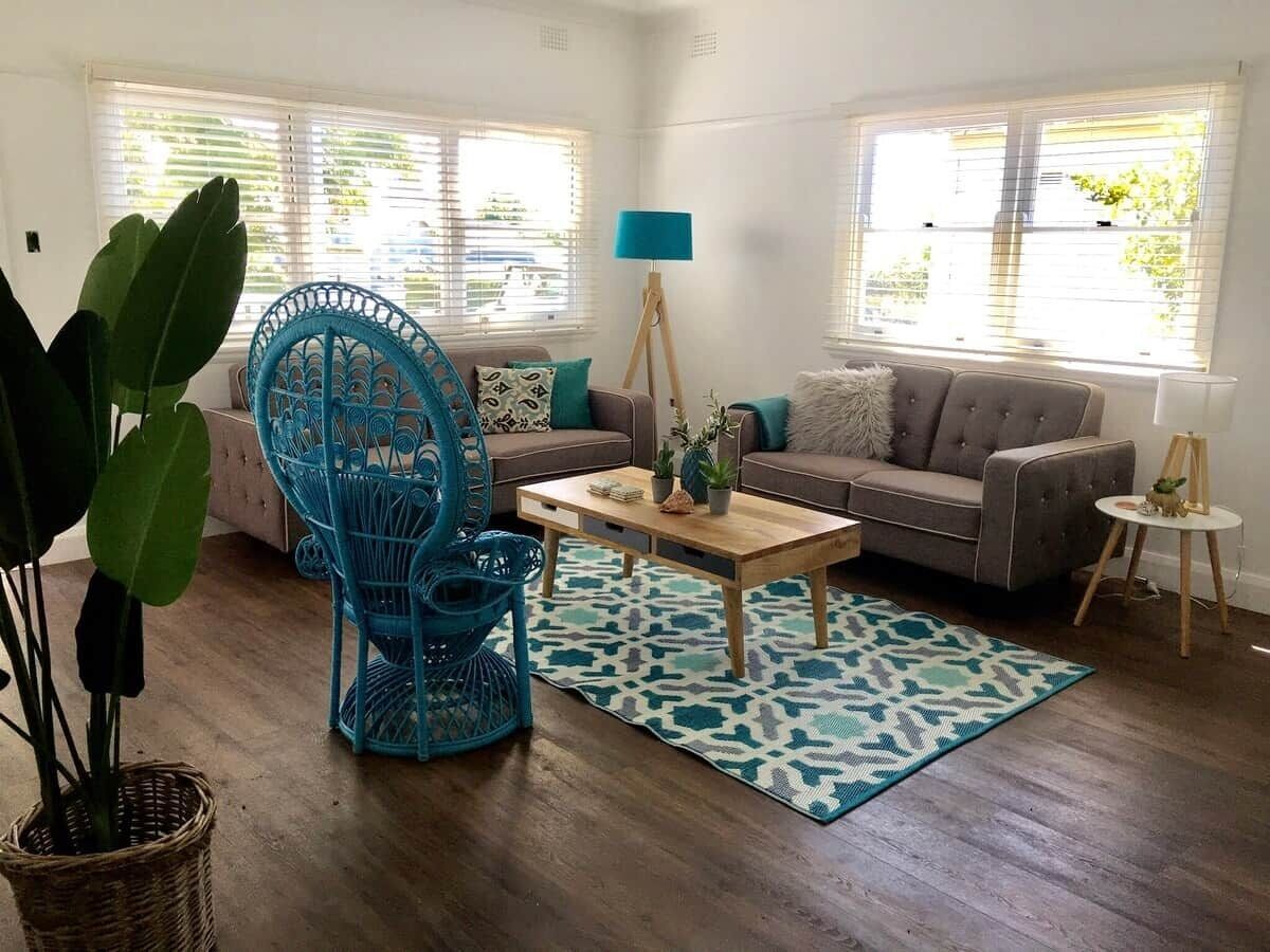 Un salon avec un canapé, une table basse, un fauteuil bleu et un tapis à motifs.