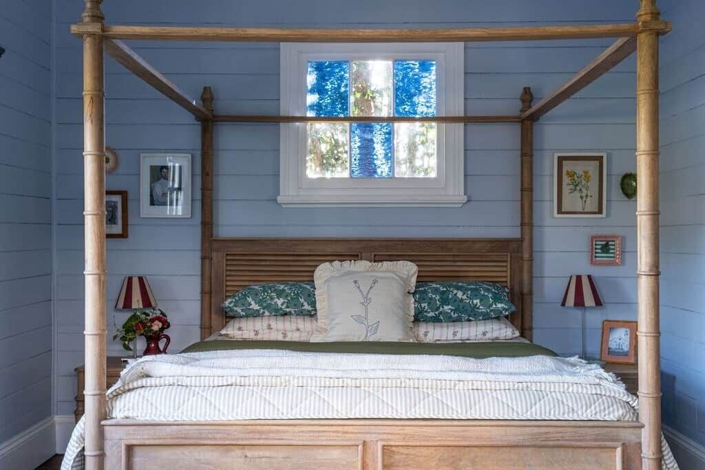 Un lit à baldaquin avec une tête de lit en bois, une fenêtre au-dessus et un mur orné de tableaux encadrés.