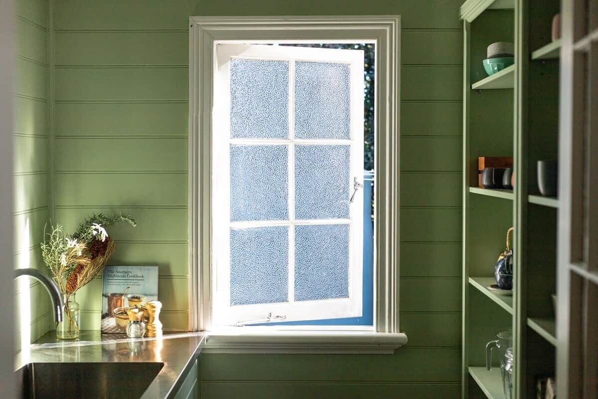 A kitchen with a window, a sink, and a shelf with kitchenware.