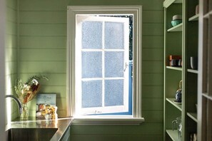 A kitchen with a window, a sink, and a shelf with kitchenware.