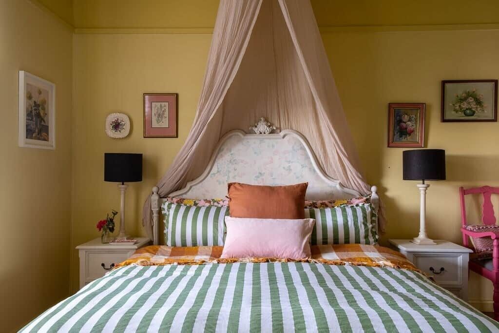 A bed with a canopy, striped bedding, and two bedside lamps.