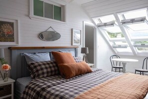 Une chambre à coucher comprenant un lit, une table de chevet, une lampe, un miroir et une fenêtre avec des lucarnes.