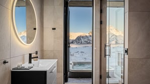 A modern bathroom with a large mirror, a bathtub, and a view of a snowy landscape through an open door. - New Luxury Designer Cabin in Lofoten (Nordland)