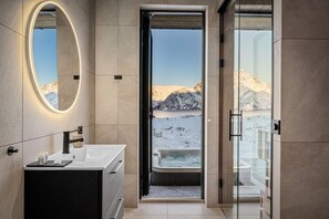 Ein modernes Badezimmer mit einem großen Spiegel, einer Badewanne und Blick auf eine verschneite Landschaft durch eine geöffnete Tür.
