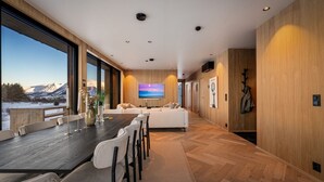 A modern interior with a large dining table, seating, a sofa, and a TV screen. - New Luxury Designer Cabin in Lofoten (Nordland)