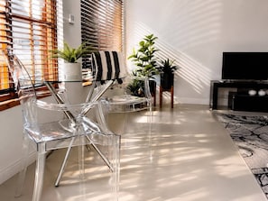 A modern living room with clear chairs, a striped towel, potted plants, and a TV stand. - Stylish Parkhurst Cottage  Walk to 4th Ave (Johannesburg)