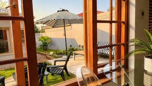 A room with a glass table, a black chair, and a striped umbrella outside.