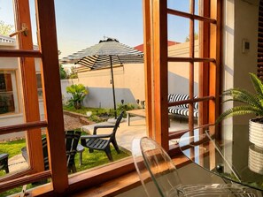 A room with a glass table, a black chair, and a striped umbrella outside.