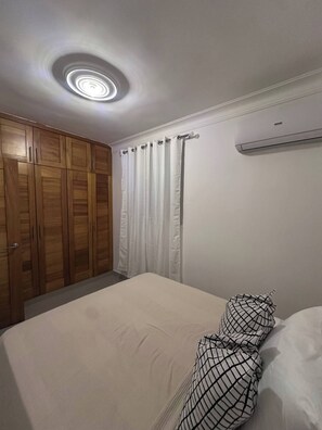 Una camera da letto con un letto, un armadio, una tenda e una lampada a soffitto.