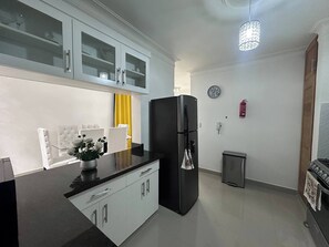 Eine moderne Küche mit einem schwarzen Kühlschrank, weißen Schränken, einem gelben Vorhang und einer Uhr an der Wand.