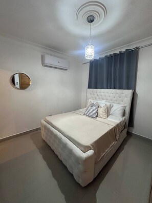 Ein Schlafzimmer mit Bett, rundem Spiegel, Klimaanlage und Pendelleuchte.