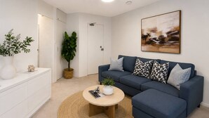 A modern living room with a blue sofa, a round coffee table, a white cabinet, and a large abstract painting on the wall. - Trendy Studio Apartment with harbour bridge views (Kirribilli)
