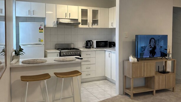 A modern kitchen with white cabinetry, a gas stove, a microwave, and a TV on a wooden stand. - Trendy Studio Apartment with harbour bridge views (Kirribilli)