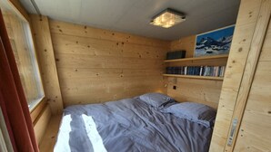 Ett litet, trärum med en säng, ett fönster med gardiner och en hylla med böcker.