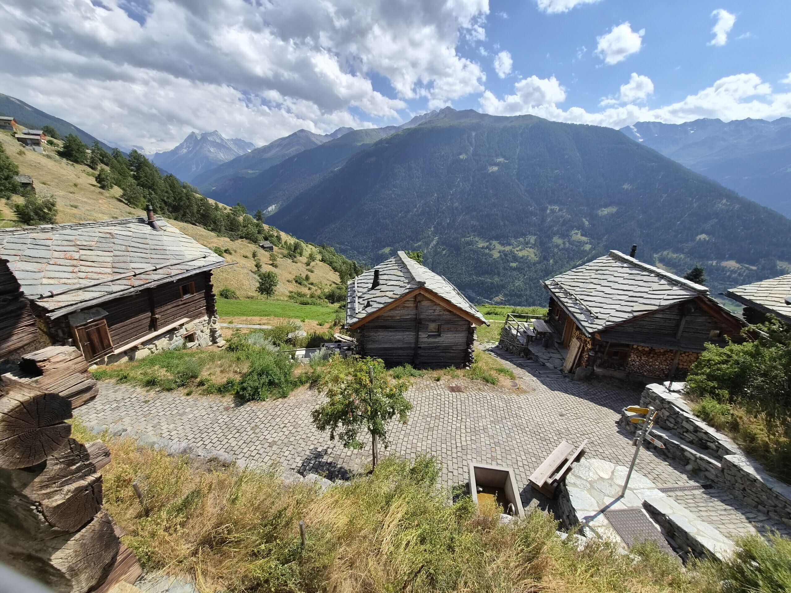 Un pueblo de montaña con casas de madera tradicionales, senderos de piedra y vistas a montañas distantes.