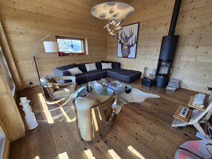 Ein gemütliches Blockhaus-Interieur mit einer Eckcouch, einem Glastisch und einem Kamin.